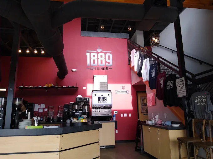 1889 Coffee House interior — espresso bar, branded red wall, and loft staircase