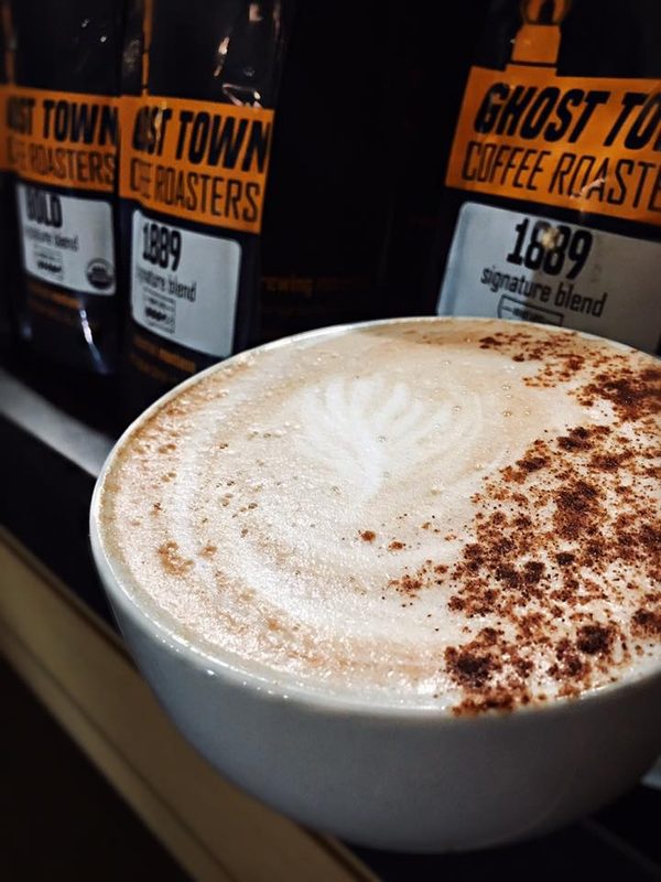 Latte with latte art alongside Ghost Town Coffee Roasters 1889 Signature Blend bags